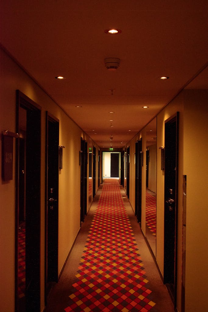 Dimly lit hotel corridor featuring vibrant checkered carpet and modern door design.